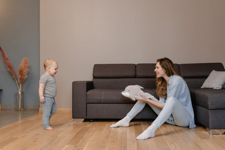 A joyful moment between a mother and her baby playing on the living room floor with a toy dolphin.